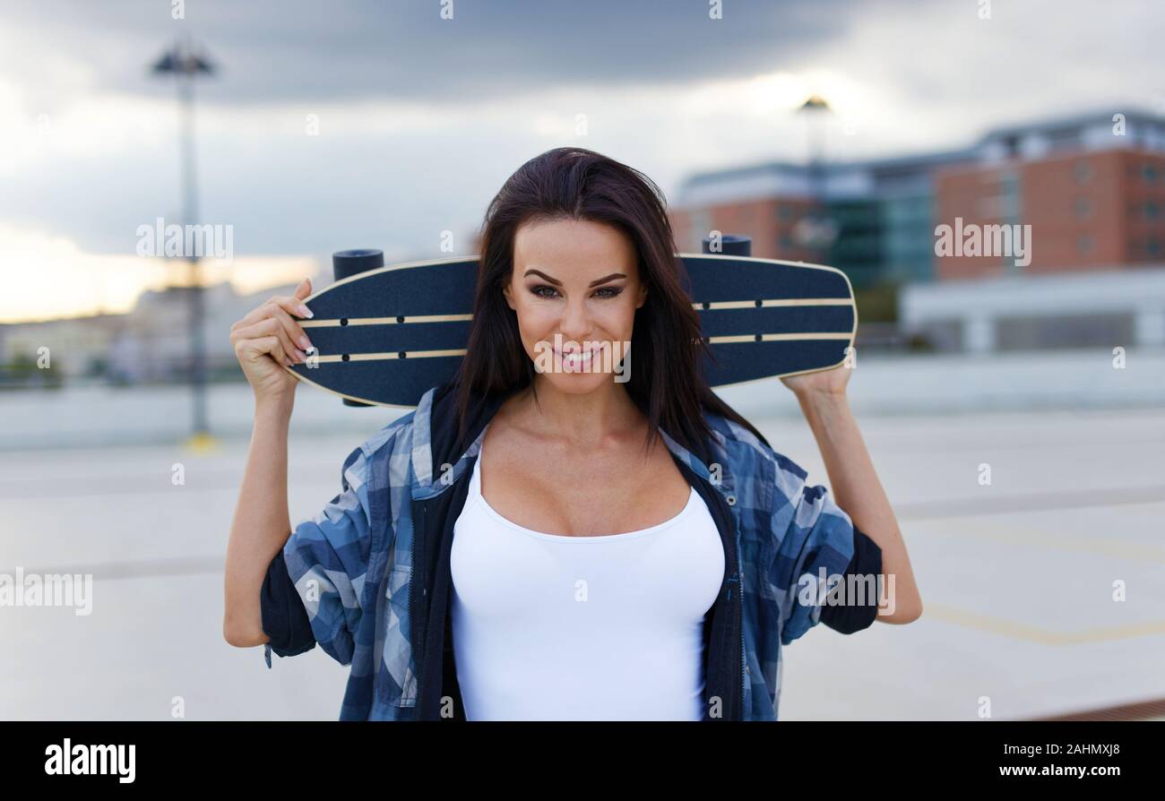 20s trendy urban woman holding longboard behind her head Stock Photo