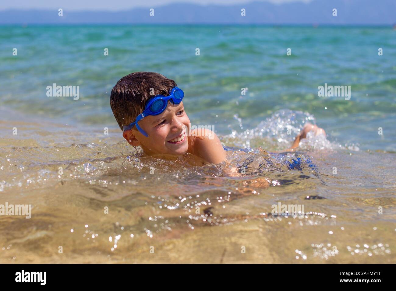 Little kid lying on sand in sea water at beach, summer holiday Stock Photo