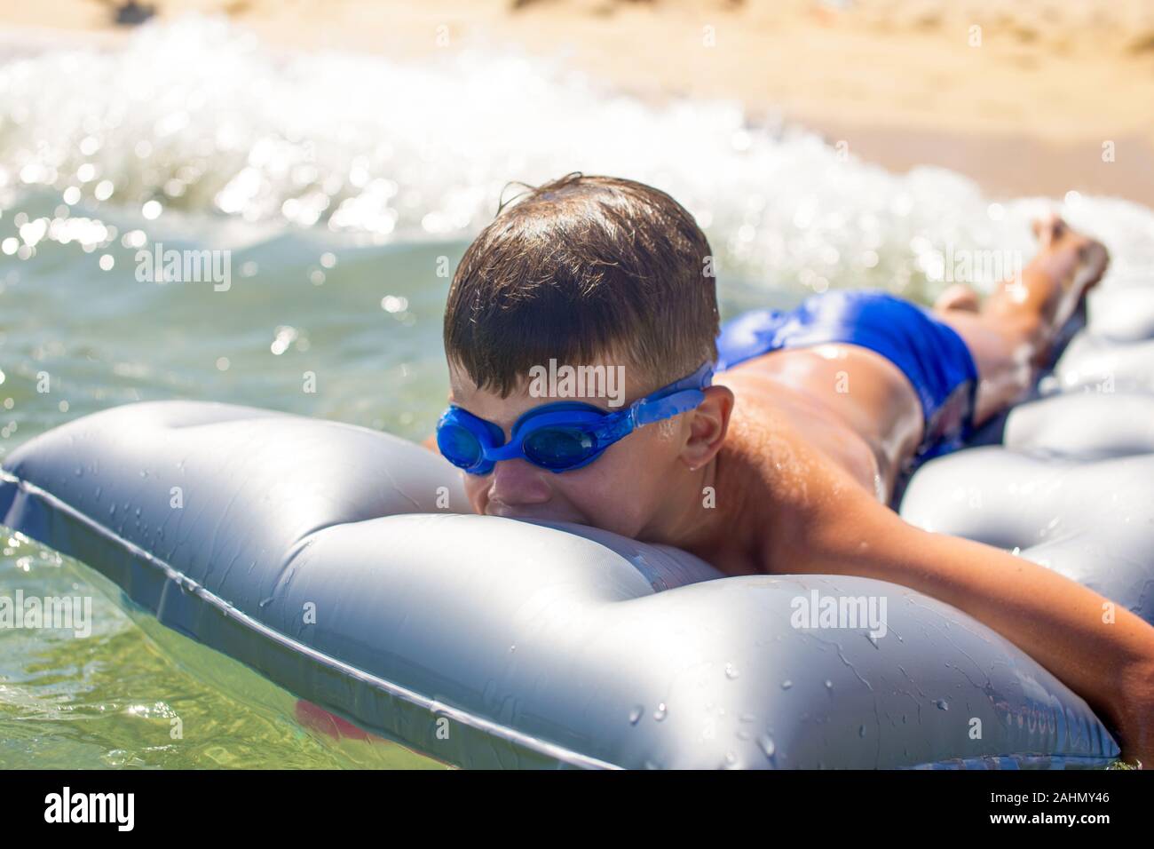 Happy little kid in goggles lying on air water mattress in sea, summer