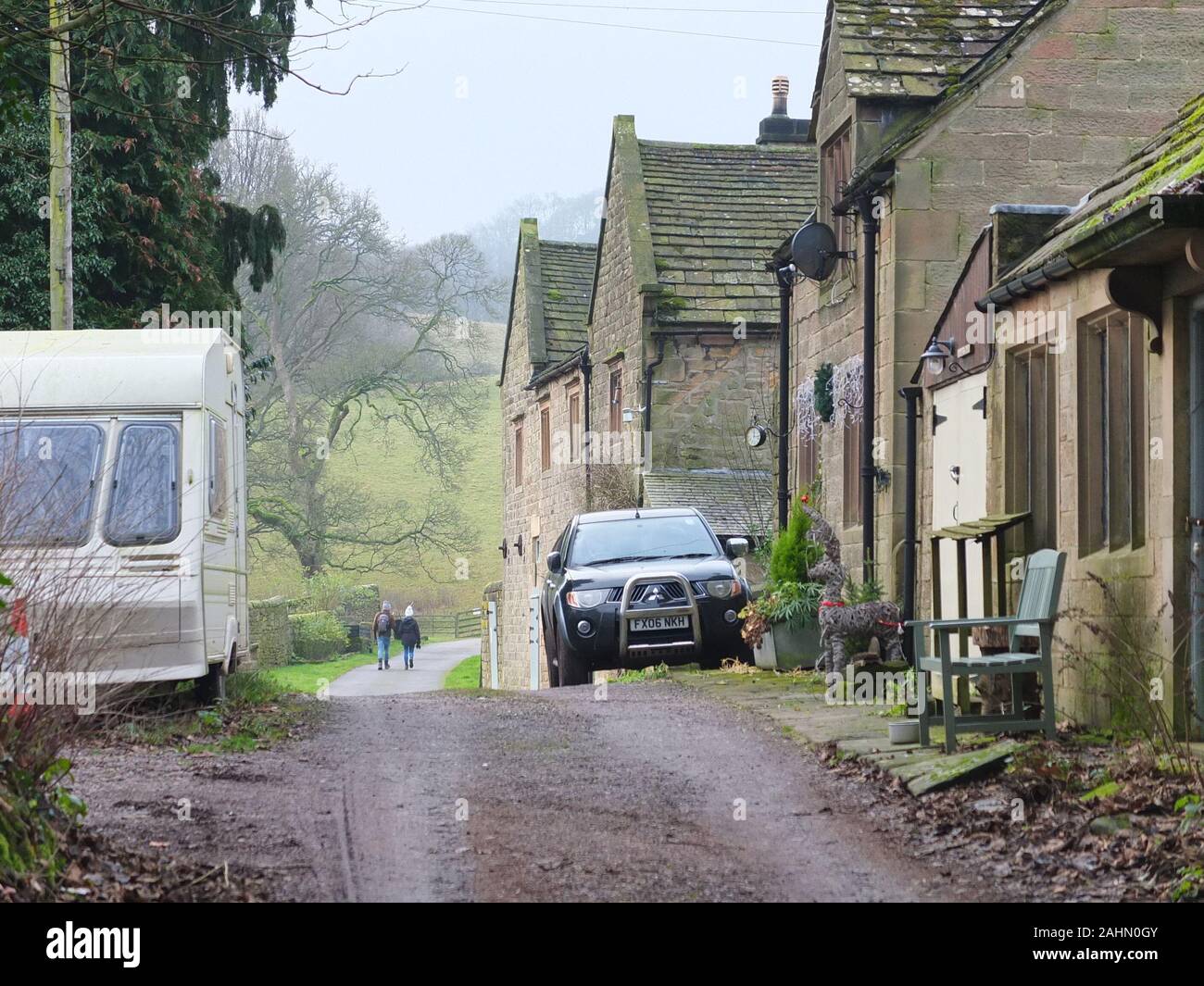 In the distance a couple of young ramblers pass by Stanton Woodhouse farm near Rowsley in the Derbyshire Peak District. A caravan parked in foreground Stock Photo