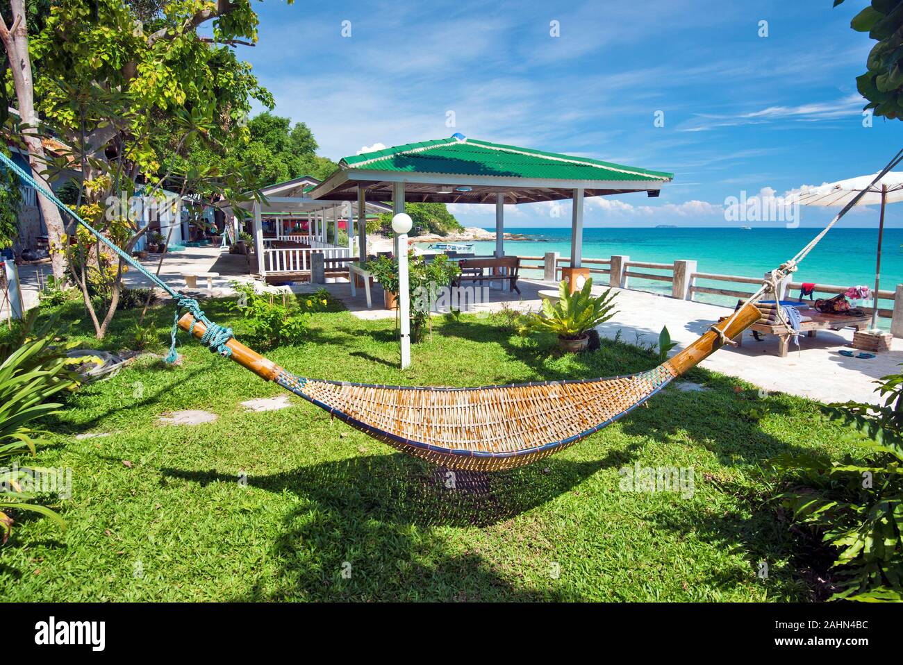 Relaxation environment in tropical beach resort, the hammock is at foreground and the sea coastline is at background. Ko Samet island, Thailand. Stock Photo