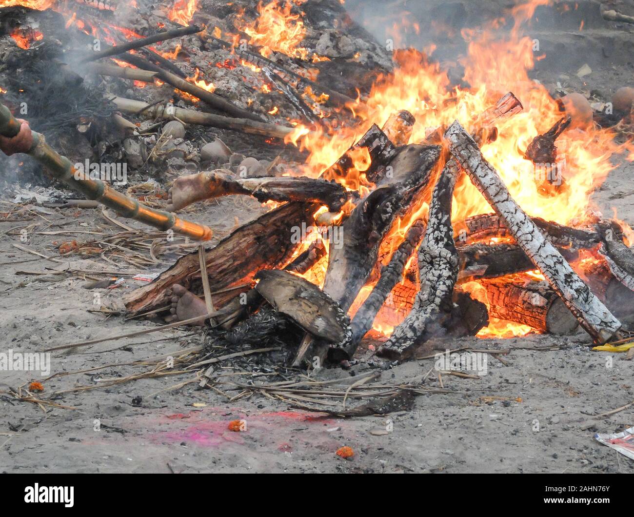 The intense heat,smoke and odors are overwhelming as a worker nearby tends a pyre with a bamboo pole and body parts are visible while Hindu corpses ar Stock Photo