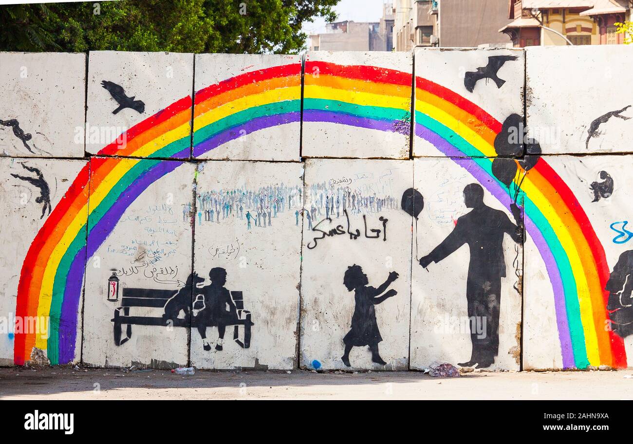 Egypt, Cairo, graffiti of the Egyptian revolution on a wall blocking a street. An adult gives a balloon to a child, over a rainbow. Stock Photo