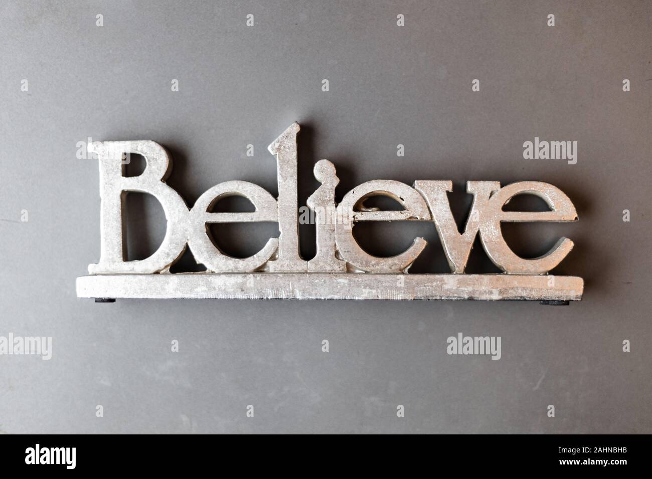 Shiny silver believe sign top down shot on matte grey background Stock Photo