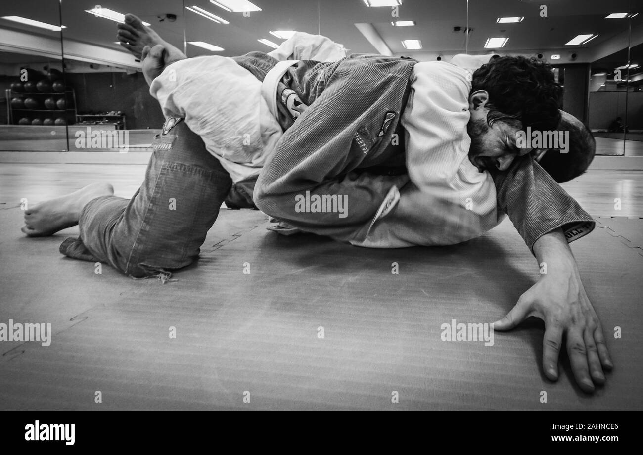 Two young men practice Brazilian Jiu-Jitsu sparring, a grappling type martial arts with a kimono gi - NOT STAGED. Man tapping out Stock Photo