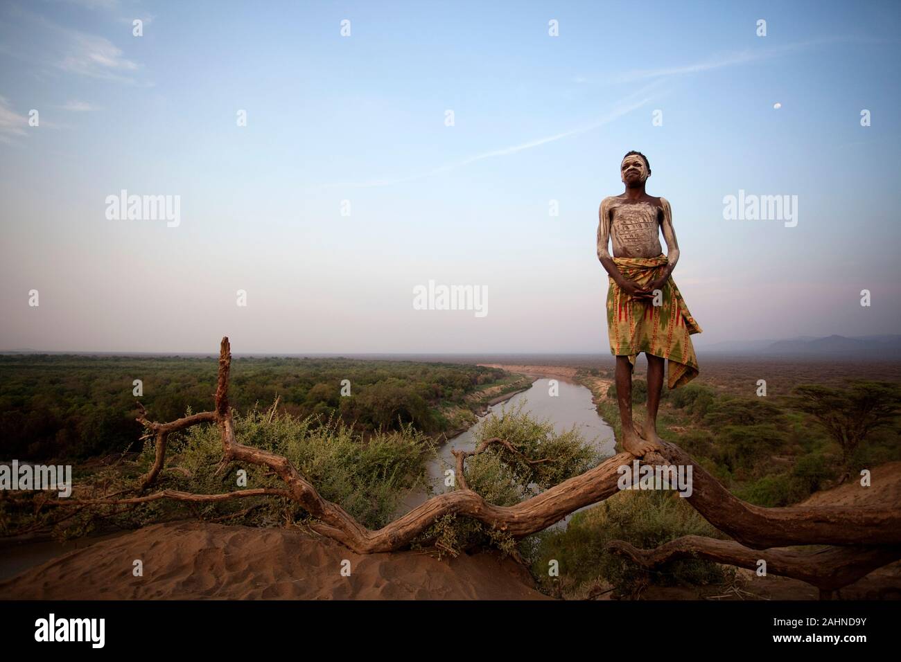 Karo tribe, Young tribal Karo boy with traditionally painted face standing on a branch above the omo river, Omo valley, Ethiopia, Africa Stock Photo