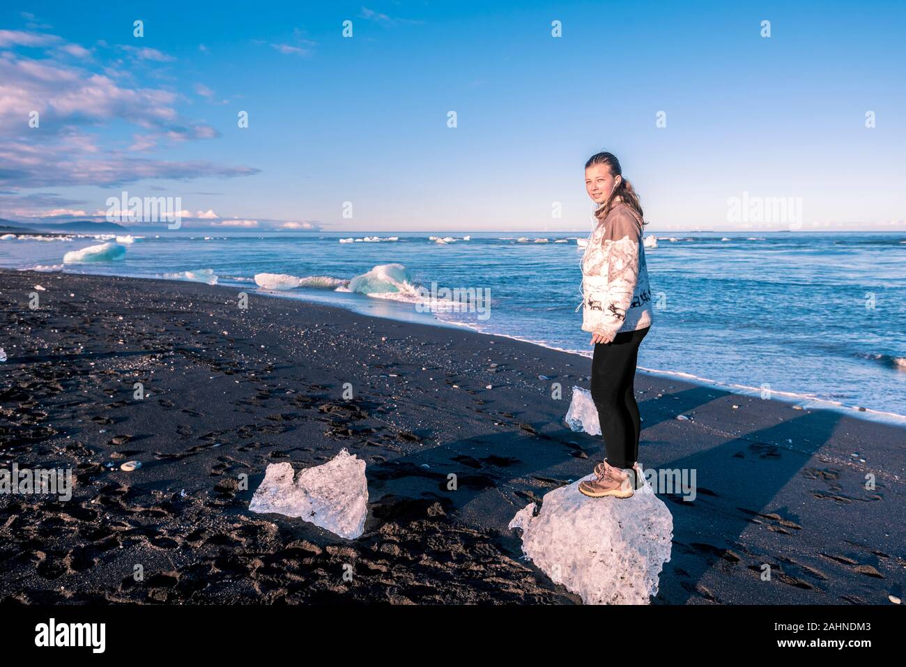 Girl teenager is staying in the small icebergs in the border of Atlantic Ocean, close to Jokulsarlon glacier lagoon in Southeastern Iceland. Stock Photo