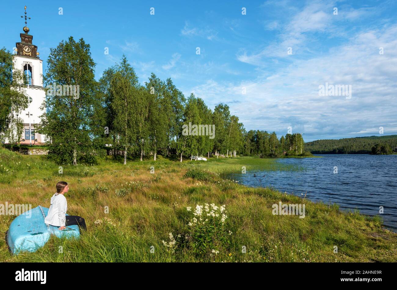 Girl is sitting in on returned bark and looking at Storan-Osterdalalven lake, the Protestant church of Idre village is at right background. Dalarna co Stock Photo
