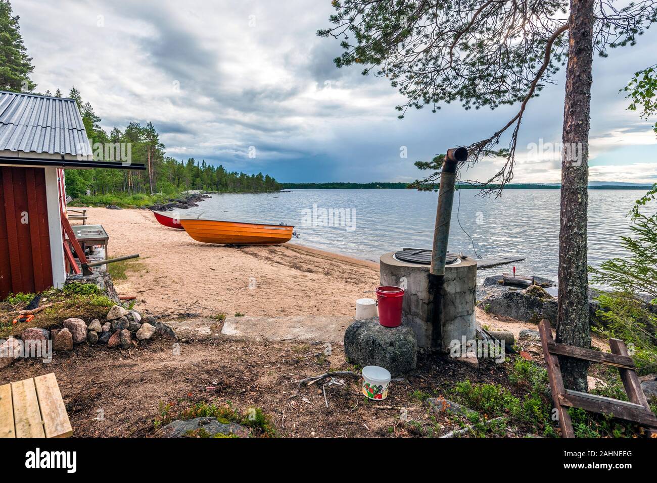 Part of the wooden house and domestic utensils in the border of Sandsjon lake in Swedish Lapland. Wood stove and motor boats are attributes of Scandin Stock Photo