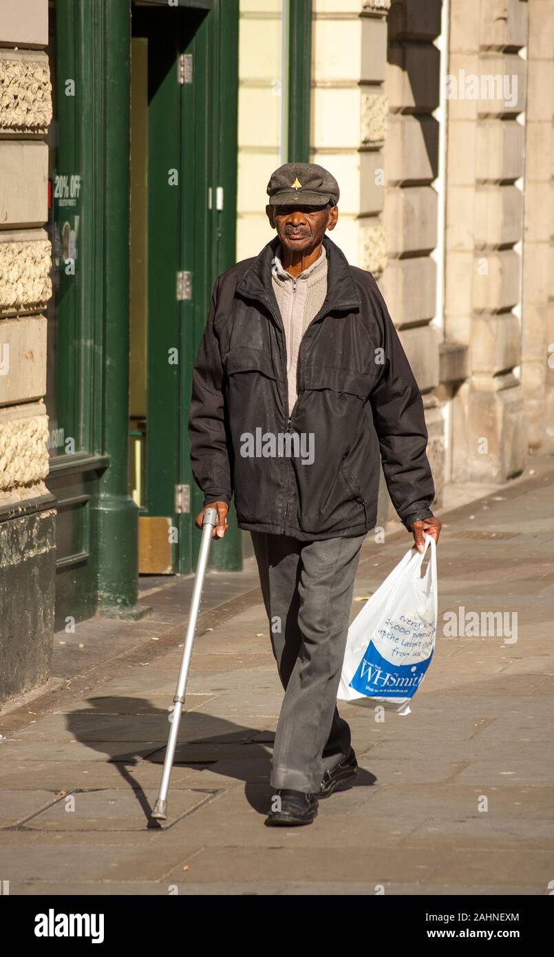 Elderly black man strolling with a walking stick and holding a carrier bag  Stock Photo - Alamy