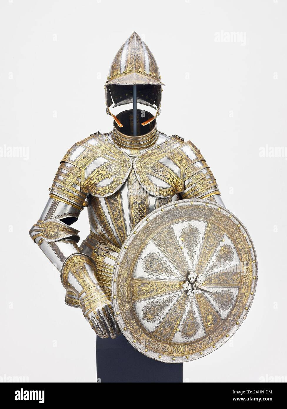 Half Armor and Targe for Service on Foot. 1585–1605. Milan. Steel, gilding, brass, and leather This is an unusually fine armor with matching targe (shield) for an infantry officer. On the breastplate and pauldrons of this ceremonial parade armor, the etched bands are embellished with interlace, trophies, fabulous beasts, and etched medallions that enclose classical figures reminiscent of Roman heroes. The etched radiating bands retain their original gilded surface, which contrasts effectively with adjacent areas left blackened in the forging process. Armor could be worn with costume accessorie Stock Photo