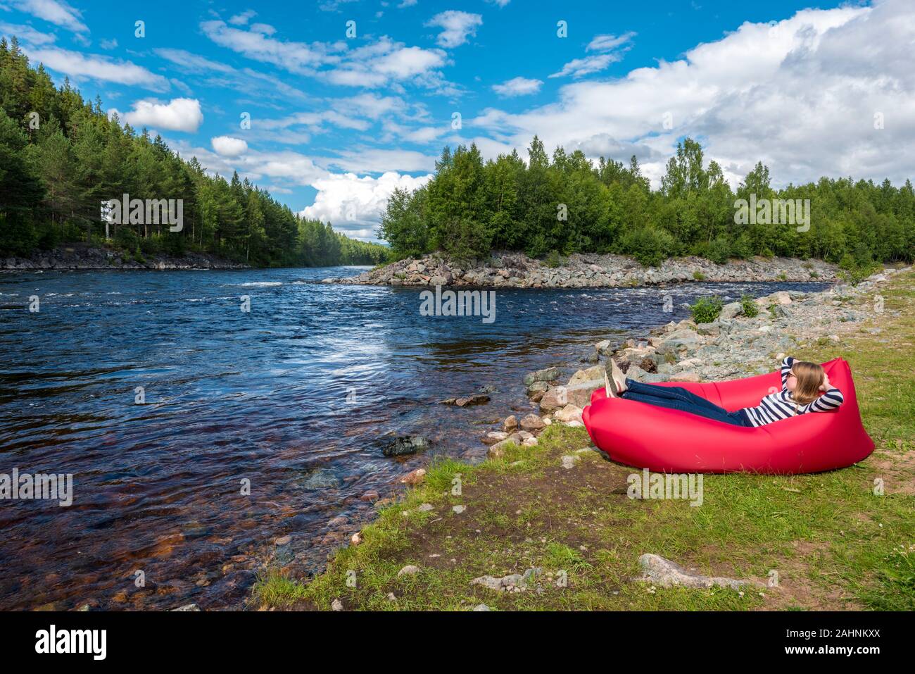 Young woman is relaxing in the red airlounger in the border of Fugga river in Hedmark county of Norway. Close to Akrestrommen village in Rendalen muni Stock Photo