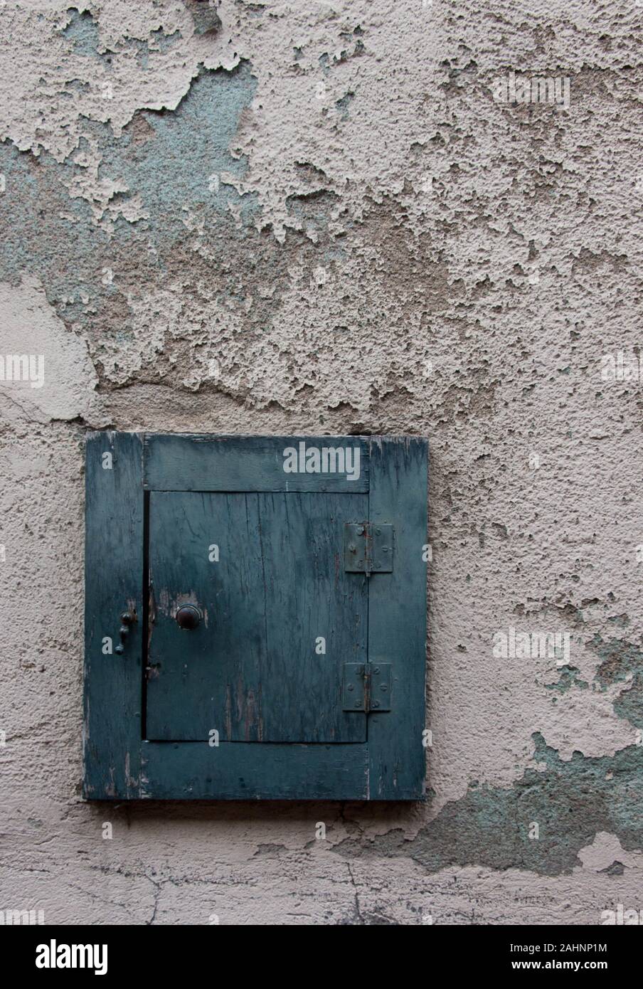 Small blue shuttered window on white peeling paint wall Stock Photo