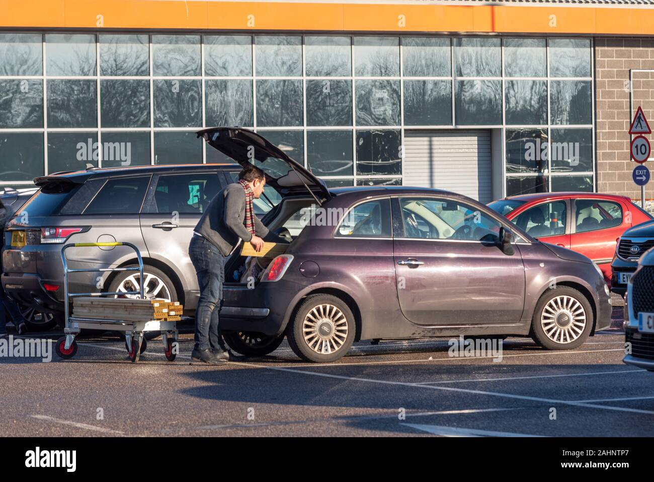 White Caucasian male loading timber into a small car at a Do It Yourself store. Inappropriate vehicle for purpose. Home improvement shop purchases Stock Photo