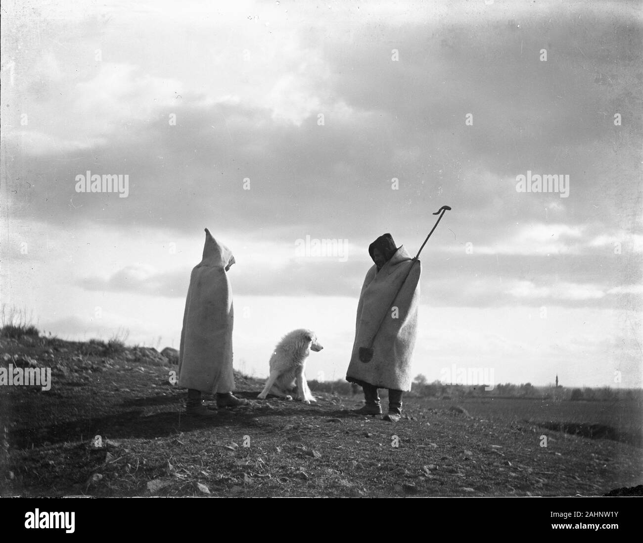 Two shepherds in traditional dress with their sheepdog in Ottoman Turkey near mediteranian sea. Atmospheric picture taken in evening sun with cloudy sky. Minaret in the background. Photograph dated around 1910-1920. Copy from a dry glass plate, originating from the Herry W. Schaefer collection. Stock Photo