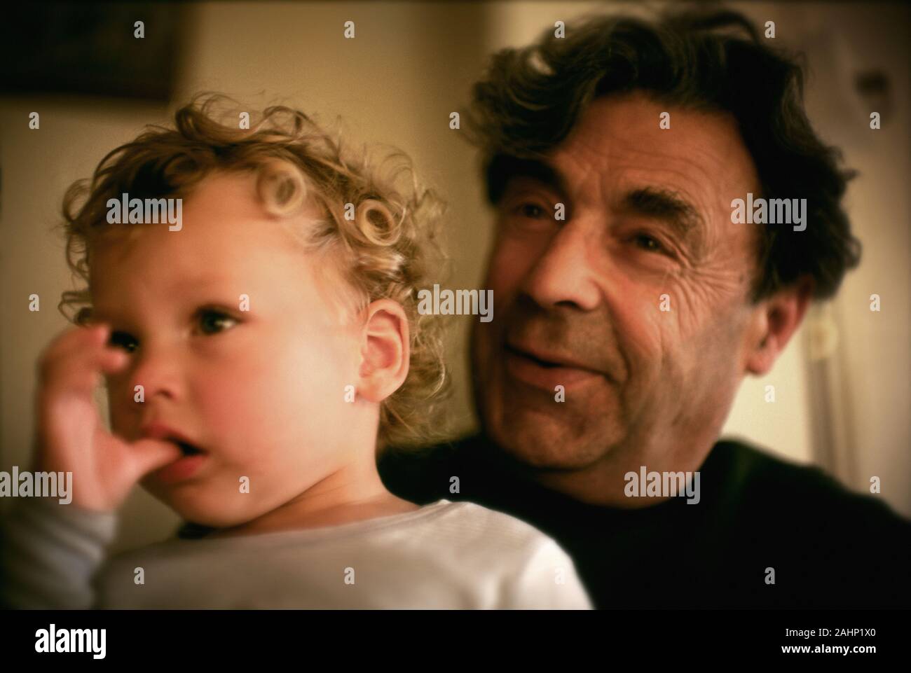 A small child sucking his thumb in his fathers arms . Stock Photo