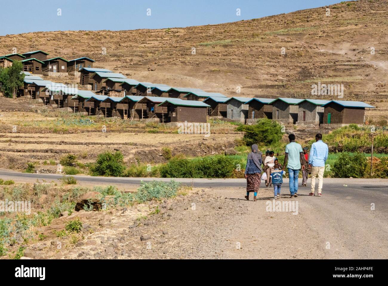 ETHIOPIA, KULMERSK,Family walking towards the new housing complex, built in traditional style with wood and mud walls but covered with mud Stock Photo