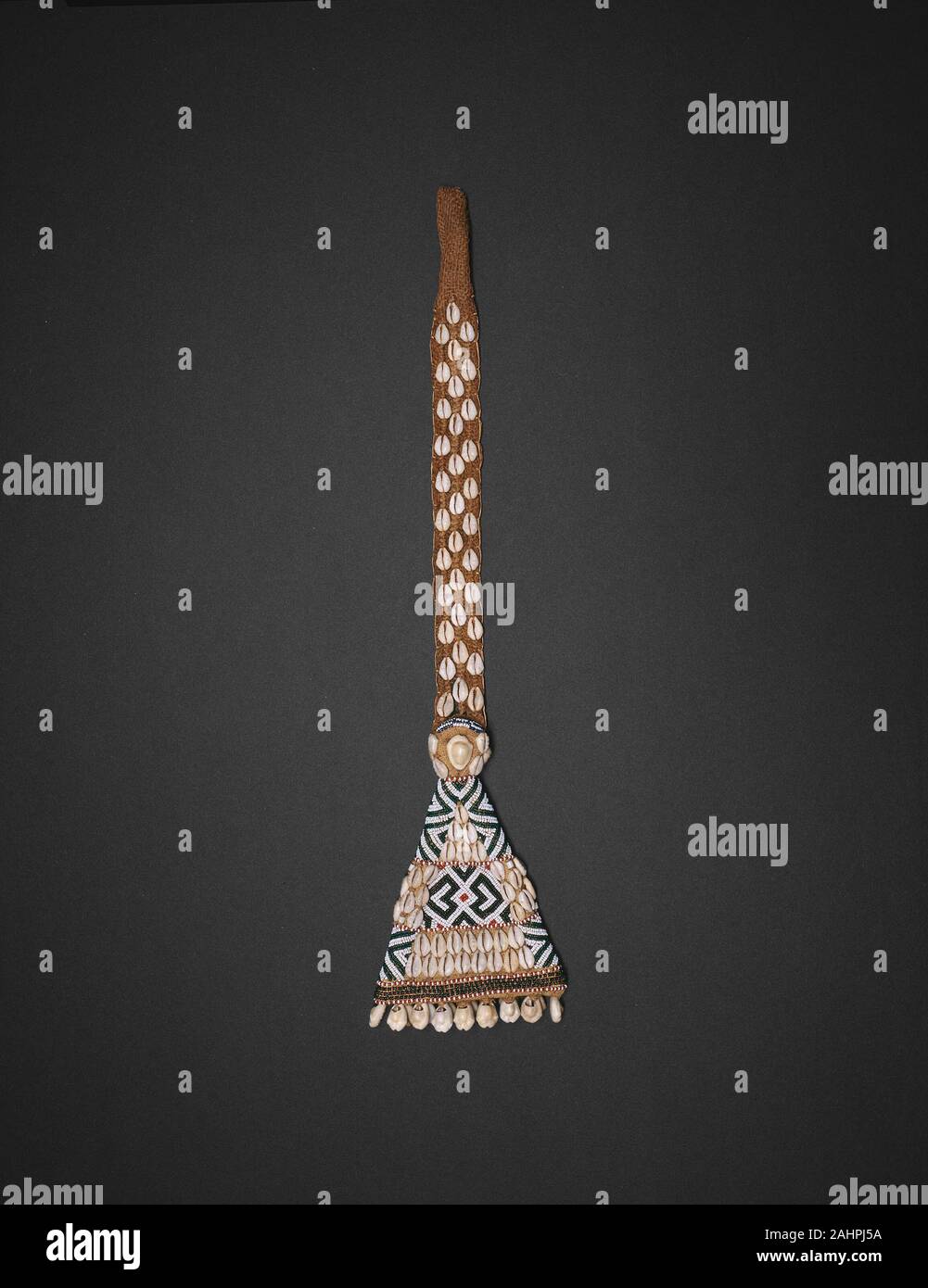 Kuba. Pendant. 1801–1900. Democratic Republic of the Congo. Jute, raffia, cowrie shells, and beads Since the inception of the Kuba Kingdom in the 16th century, individuals have signaled court rank and status with their elaborate dress. Glass beads imported from Europe and cowrie shells from the Indian Ocean have been used in the production of such accoutrements since the 18th century. Exclusively owned by men, bead- and shell-covered belts and pendants like this pre-1910 examples are still worn in combination with voluminous textile skirt-wrappers by both Kuba royalty and Kuba masqueraders. [S Stock Photo