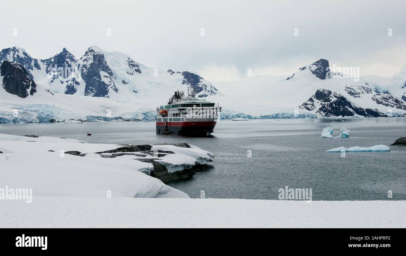 Expedition ship Fram anchored near  Petermann Island, Antarctica. On the left, you can see a small zodiac taking people to shore. Stock Photo