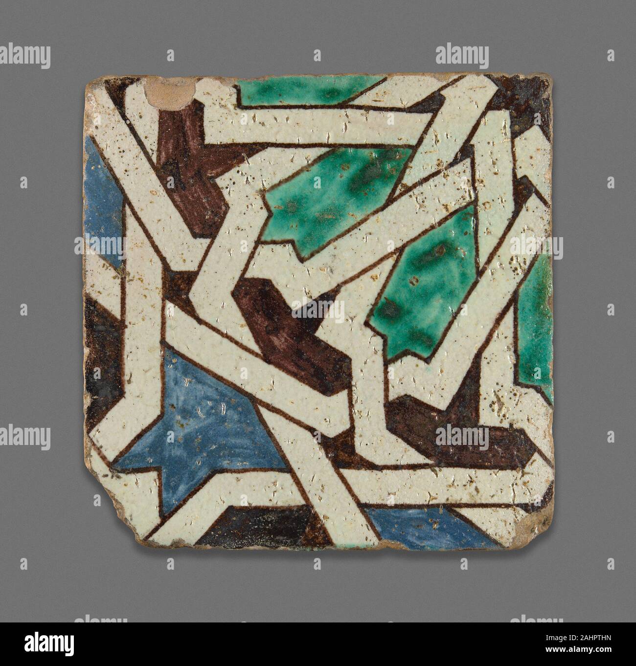 Square Tile. 1867–1899. Morocco. Polychrome pigment applied over opaque white glaze Geometric tilework comprised of individually cut pieces, or zillij, is a prominent feature of Moroccan architecture dating back more than 700 years. It is incredibly costly to make due to the skill involved in the design and layout of the mosaic. This imitation zillij tile achieves a similar effect while reducing the cost of labor and materials, and it speaks to the enduring importance of the zillij style as a highly prized art form in 19th-century Morocco. In an architectural context, numerous zilij tiles woul Stock Photo