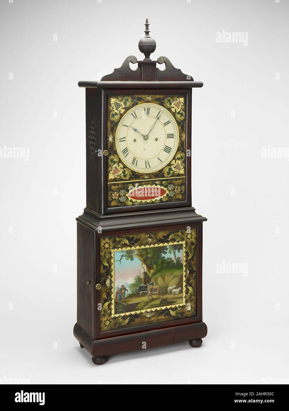 Benjamin Torrey. Shelf Clock. 1820–1840. United States. Mahogany, white pine, iron, brass, painted glass An alternative to expensive tall case clocks, shelf clocks were more affordable in the early 19th century. On this piece, Benjamin Torrey used a technique called eglomise, in which paint is applied to the back of a glass pane so that the reverse image is visible to the viewer. The romanticized pastoral scene and the decorative motif that borders both the upper and lower cases evince the design possibilities in use during the Neoclassical period. This particular clock is rare in that it reta Stock Photo
