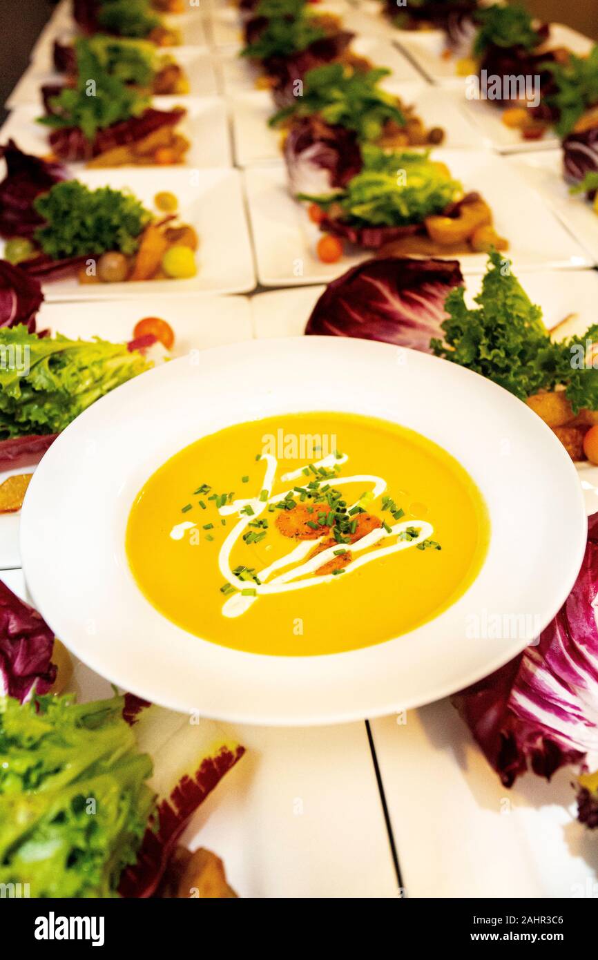 Bowl of butternut squash soup on top of cabbage,kale and tomato salads ready for a catered dinner event Stock Photo