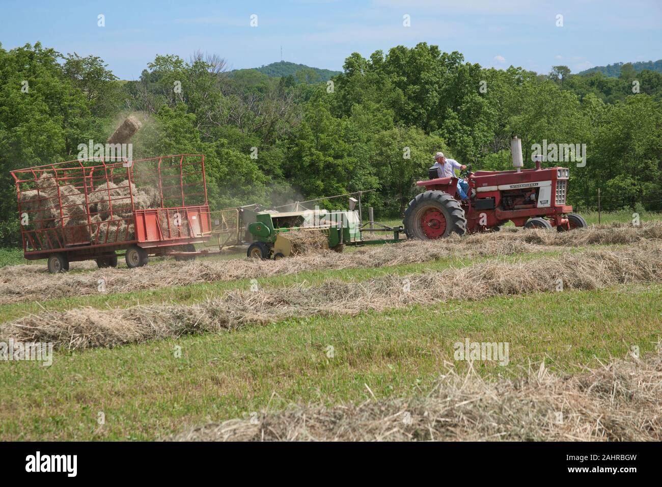 Man on International Harvester Farmall tractor, baling hay in a field with a bale flying in the air, in Galena, Illinois, USA.  (For editorial use onl Stock Photo