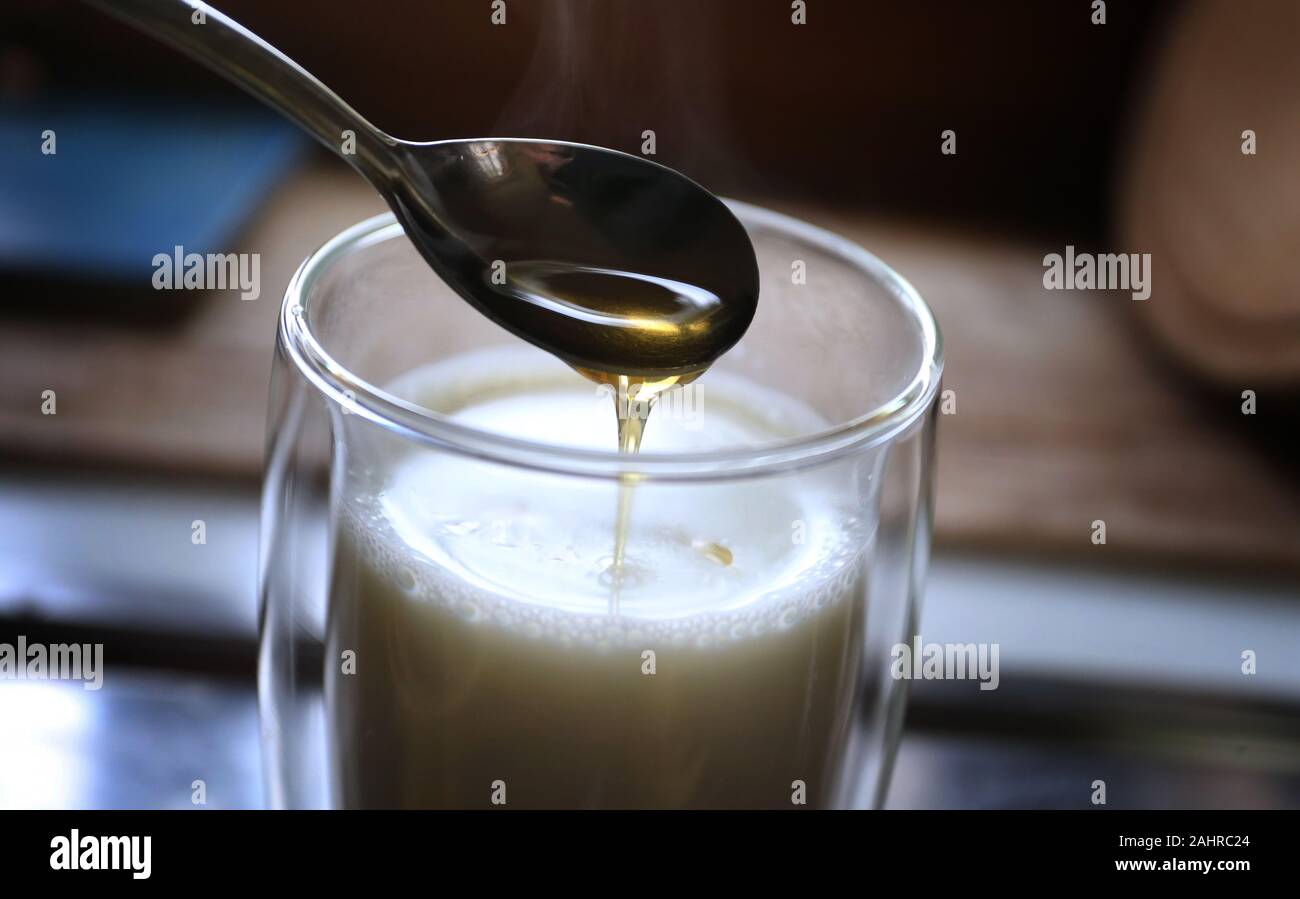 Kaufbeuren, Germany. 20th Dec, 2019. Honey flows from a spoon into a glass with hot milk. Everybody knows some home remedy that helps with colds - supposedly. Because there is not much research on household remedies. (to dpa 'Cold season: household remedies are often a boon, but hardly researched') Credit: Karl-Josef Hildenbrand/dpa/Alamy Live News Stock Photo