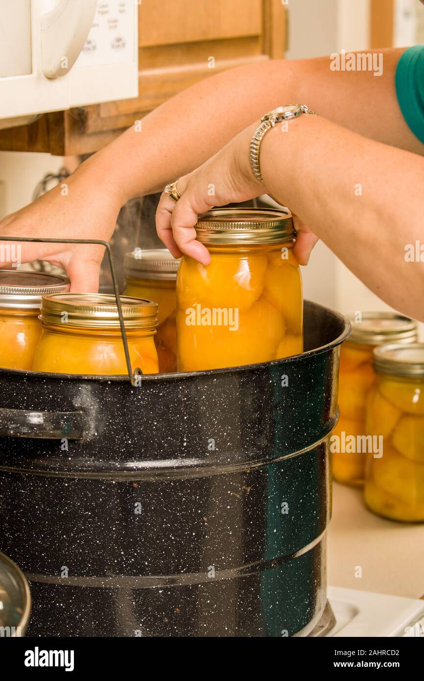 Woman placing canning jars into a rack of a hot water bath canner. The