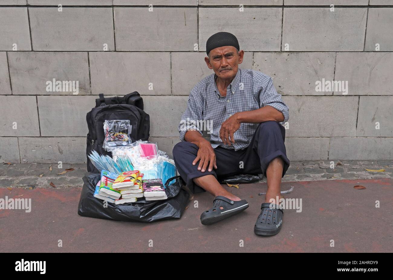 jakarta, indonesia – 2019.12.16: an old man sitting on the pavement in front of grand indonesia shopping mall selling sundry toilet articles Stock Photo