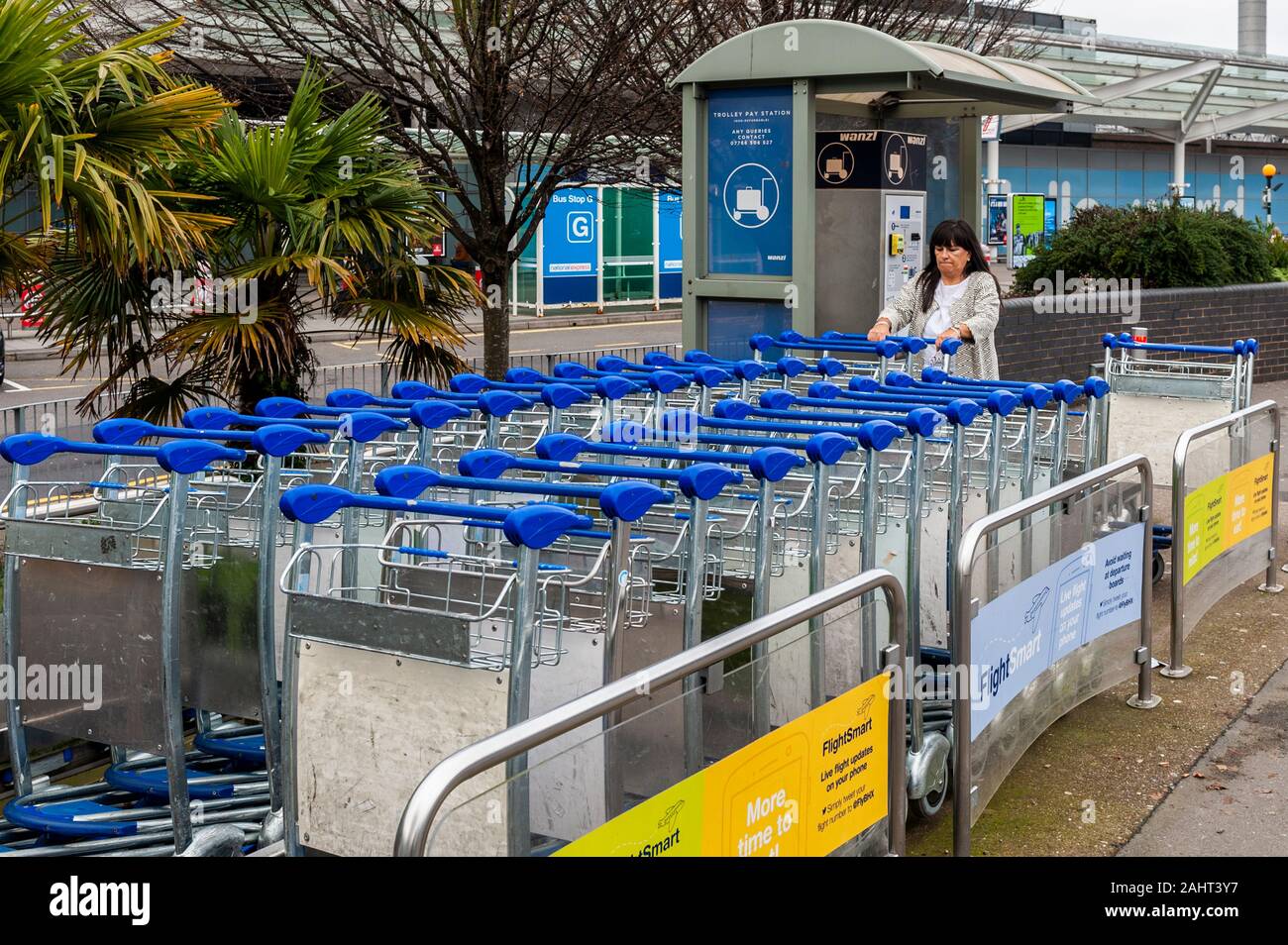 Female air traveller gets a luggage trolley for her bags at Terminal 2, Birmingham Airport, West Midlands, UK. Stock Photo