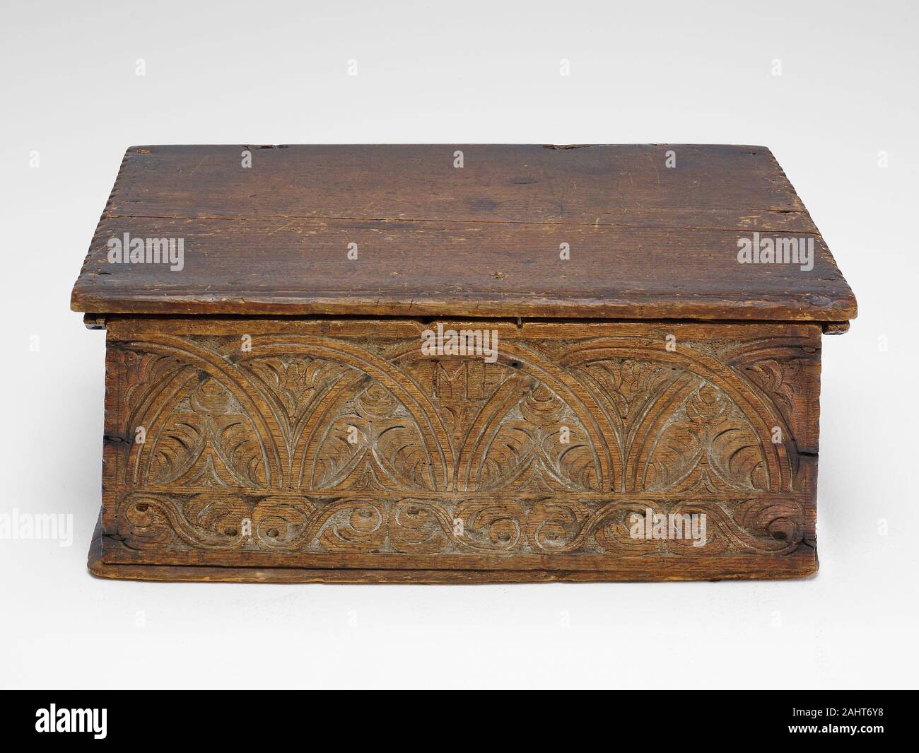 Artist unknown. Box. 1650–1700. Eastern Massachusetts. Red oak and white pine The most common object in a colonial home, a small, lidded rectangular storage box would have held personal articles, such as household items, writing implements, or a Bible. They were decorated simply, usually only on the front, with stylized plants or vegetation and geometric lines. The Art Institute’s box is segmented by an upper band of intersecting lunettes with intervening foliate leaves and a lower border with repeating floral S-scrolls. The initials M P, carved in the center of the box, are presumably those o Stock Photo