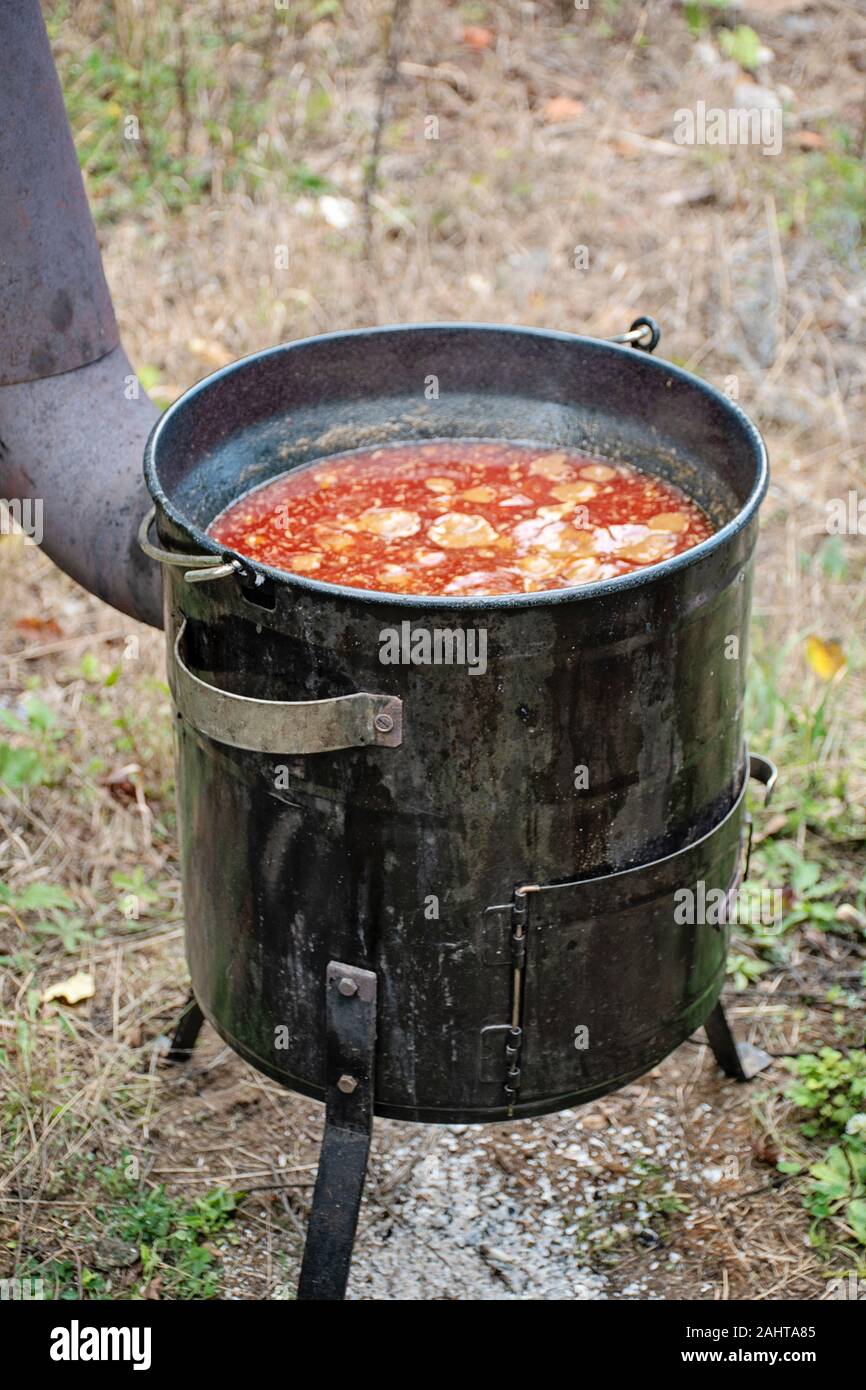 Cooking delicious kettle goulash with meet, pepper, tomatoes, onion in a large cauldron outdoors Stock Photo