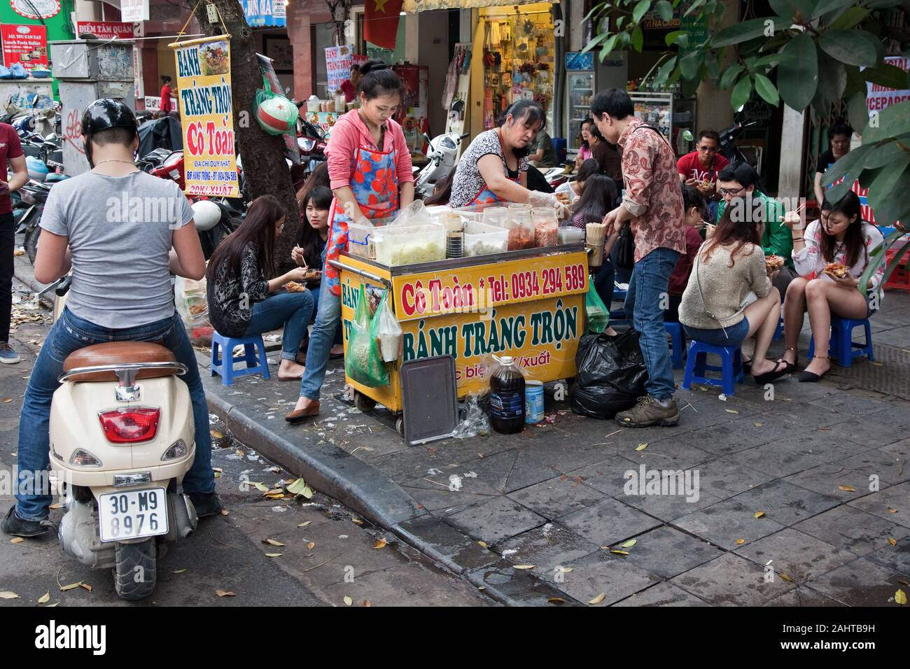 Asian people sitting on small chairs eat their lunch together at a fast food vendor Stock Photo