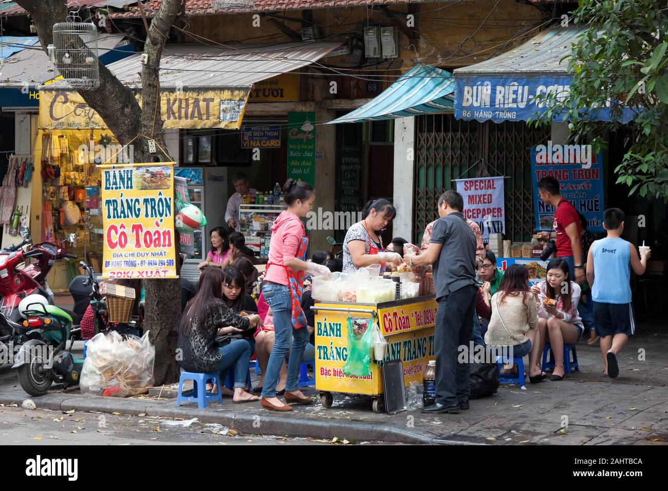 Asian people sitting on small chairs eat their lunch together at a fast food vendor Stock Photo