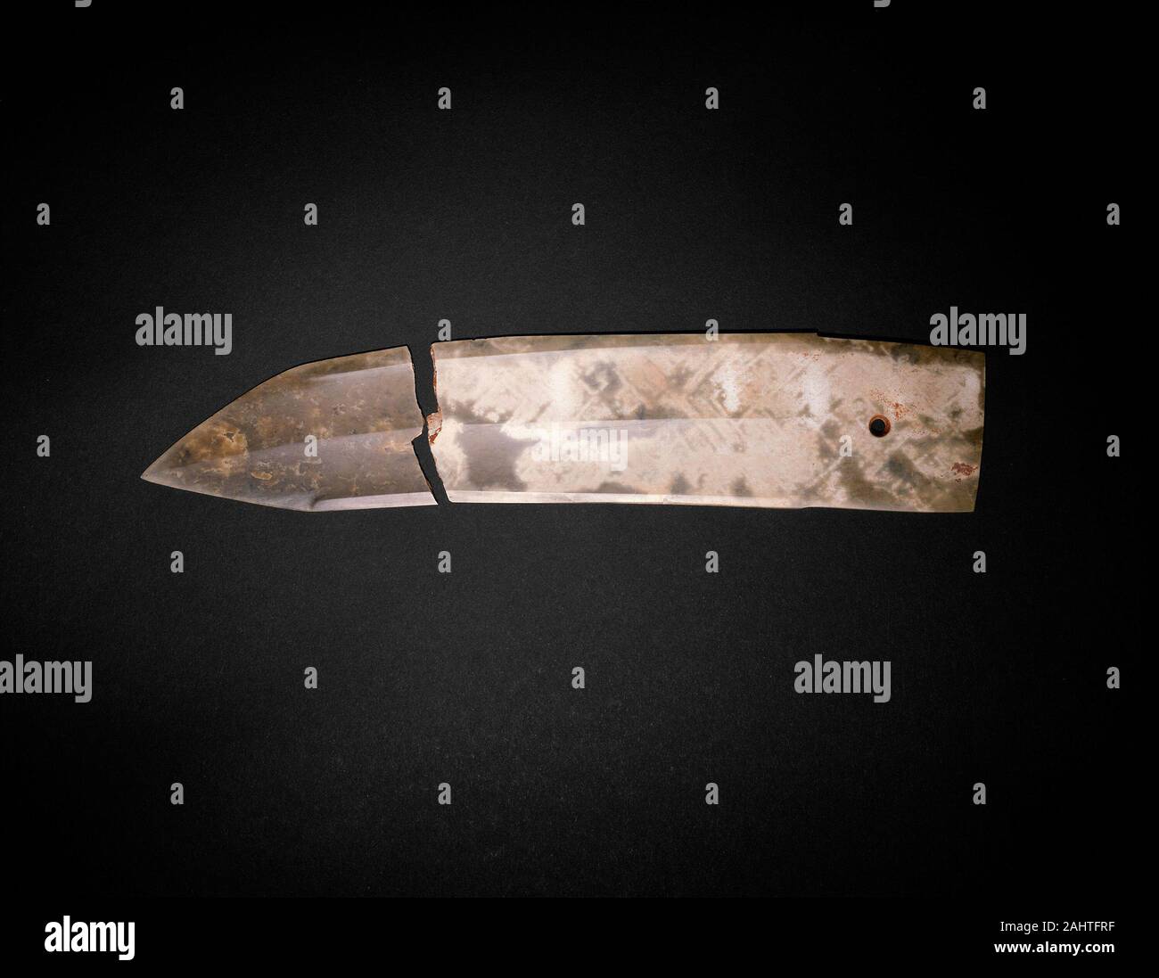 Dagger-Blade (ge). 1300 BC–1000 BC. China. Jade The earliest archaeological finds of silk in China comprise very small fragments of fabric that are datable to the 4th and 3rd millennia B.C. Silks with woven patterns are rarely preserved but can be documented about one thousand years later, primarily through ghost-like imprints on jade implements as well as bronze vessels and weapons. Before burial, these prestigious ceremonial objects were evidently wrapped in fragile but fugitive silk fabrics.Preserved near the edge of this jade blade is a three-dimensional pseudomorph (“false form”) of a squ Stock Photo