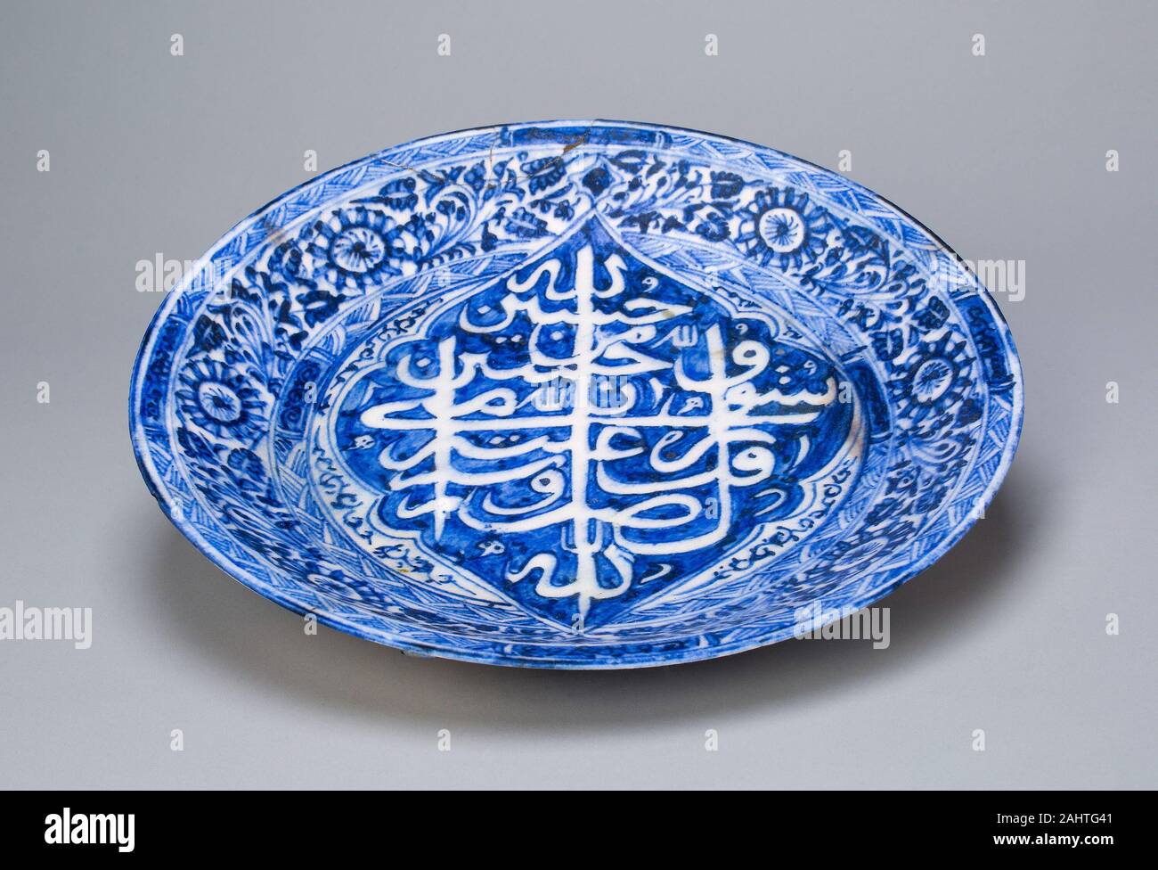 Islamic. Dish. 1822–1823. Iran. Fritware, painted in blue under a transparent glaze The color palette and naturalistic designs of this dish are a testament to the enduring influence of Chinese porcelain on ceramics of the Islamic world. This dish features floral decorations in a naturalistic Chinese style and the traditional blue-and-white color scheme. The central calligraphic motif of the dish, offering pious sayings, is written in Arabic script, but its shape recalls Chinese characters. Chinese influence on Islamic ceramics can be seen as early as the 9th century, and it continued well into Stock Photo