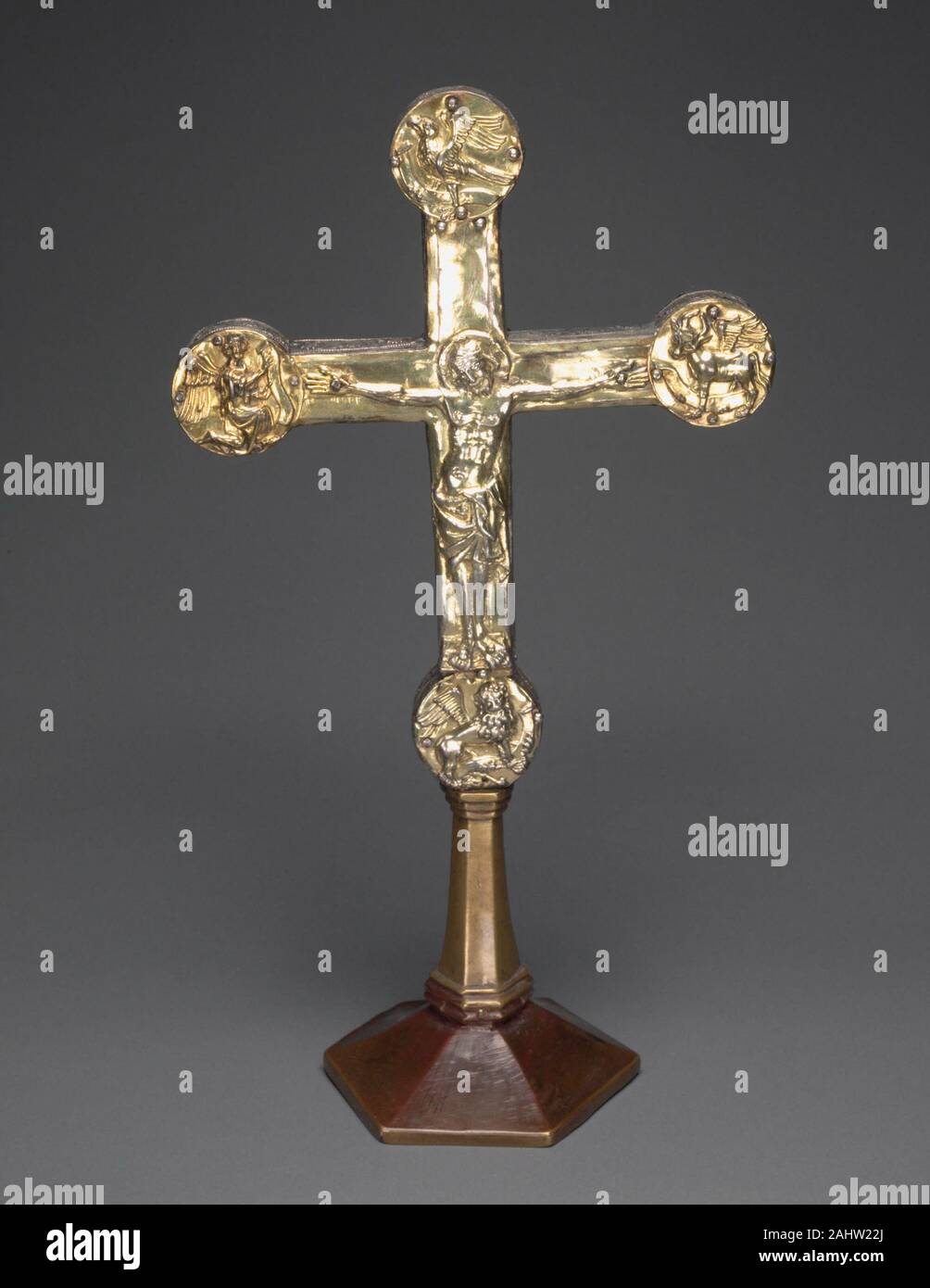 Altar Cross. 1320–1330. Brunswick. Silver gilt over a wooden core; foot copper gilt This silver-gilt cross with the figure of the crucified Christ was meant to be placed on an altar. Each arm of the cross terminates with a roundel containing the symbols of the four Evangelists the angel for Saint Matthew, the lion for Saint Mark, the ox for Saint Luke, and the eagle for Saint John the Evangelist. These four images were cast from the same molds used for the Evangelist symbols that decorate a silver book cover made for a liturgical manuscript written in 1326, now housed in the Kunstgewerbemuseum Stock Photo