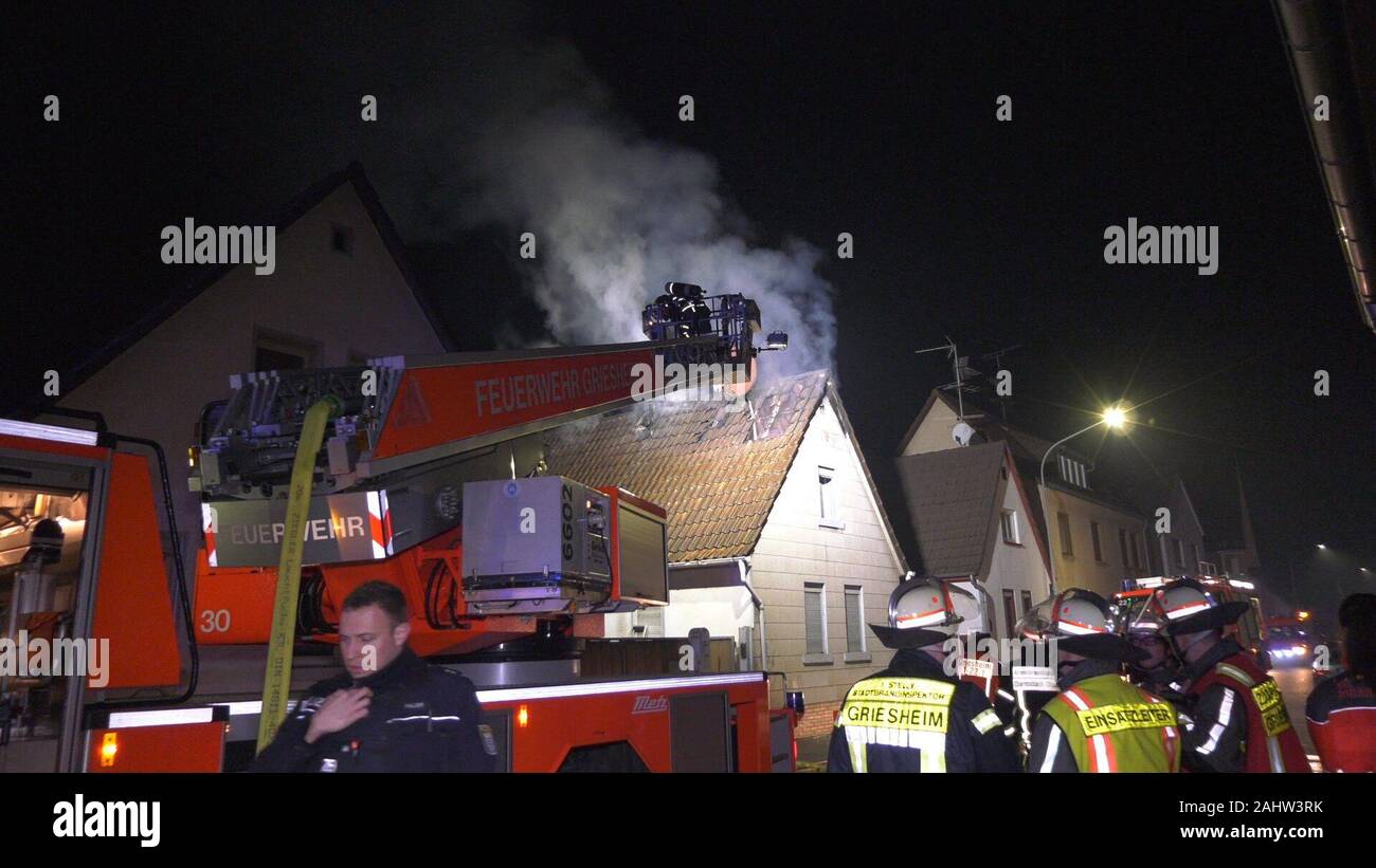 01 January 2020, Griesheim: Rescue workers of the fire brigade extinguish a fire on the roof truss of an apartment building in Schöneweibergasse. The roof truss was probably set on fire by a New Year's Eve rocket which caught fire there. The rapid intervention of the fire brigade prevented the fire from spreading to the entire house. (to dpa: 'Roof truss fire after midnight: house uninhabitable') Photo: Alexander Keutz/-/dpa Stock Photo