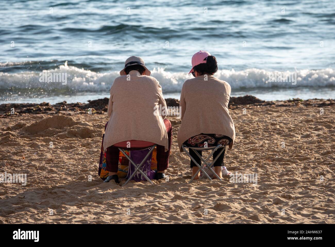 Benidorm, Alicante Province, Spain. 1st January 2020. Tourists and locals enjoy the warm, sunny weather on Levante beach on New Years Day. Two women sitting on small beach chairs with backs to camera. Credit: Mick Flynn/Alamy Live News Stock Photo