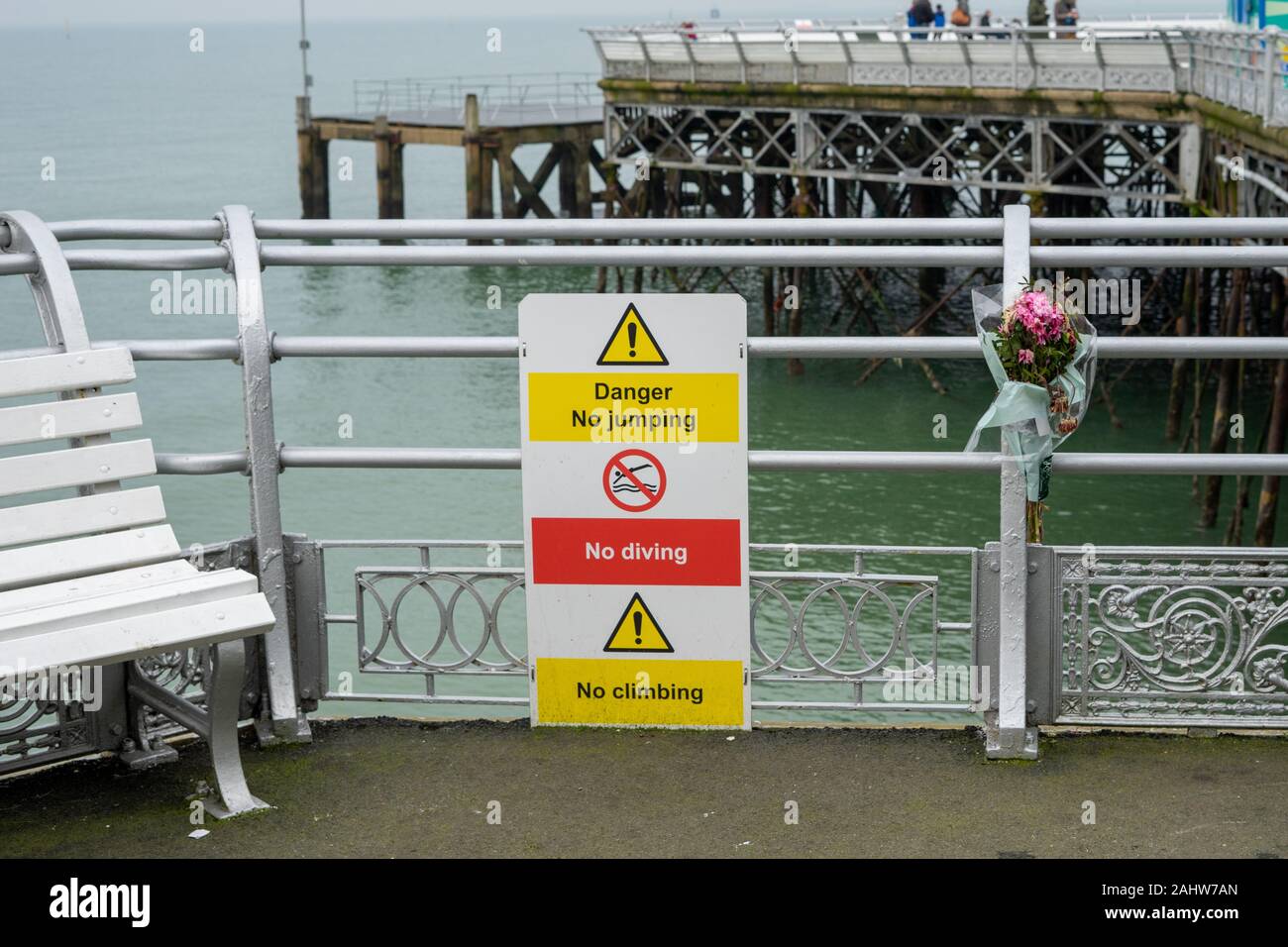 A sign on a pier stating no jumping and no diving, a bouquet of flowers has been placed next to the sign in remembrance of somebody that died Stock Photo