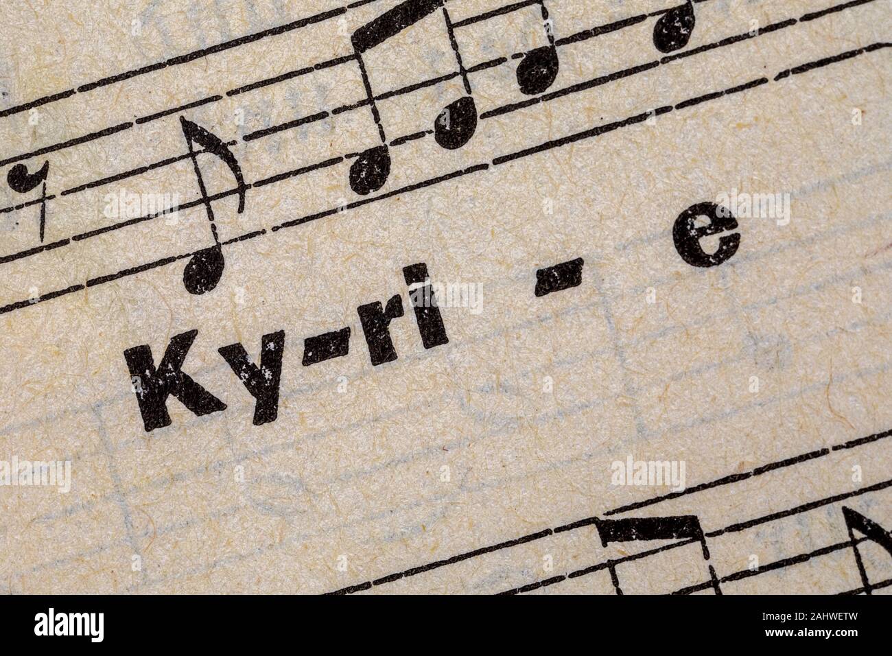 printed word Kyrie on old handmade paper with music notes Stock Photo