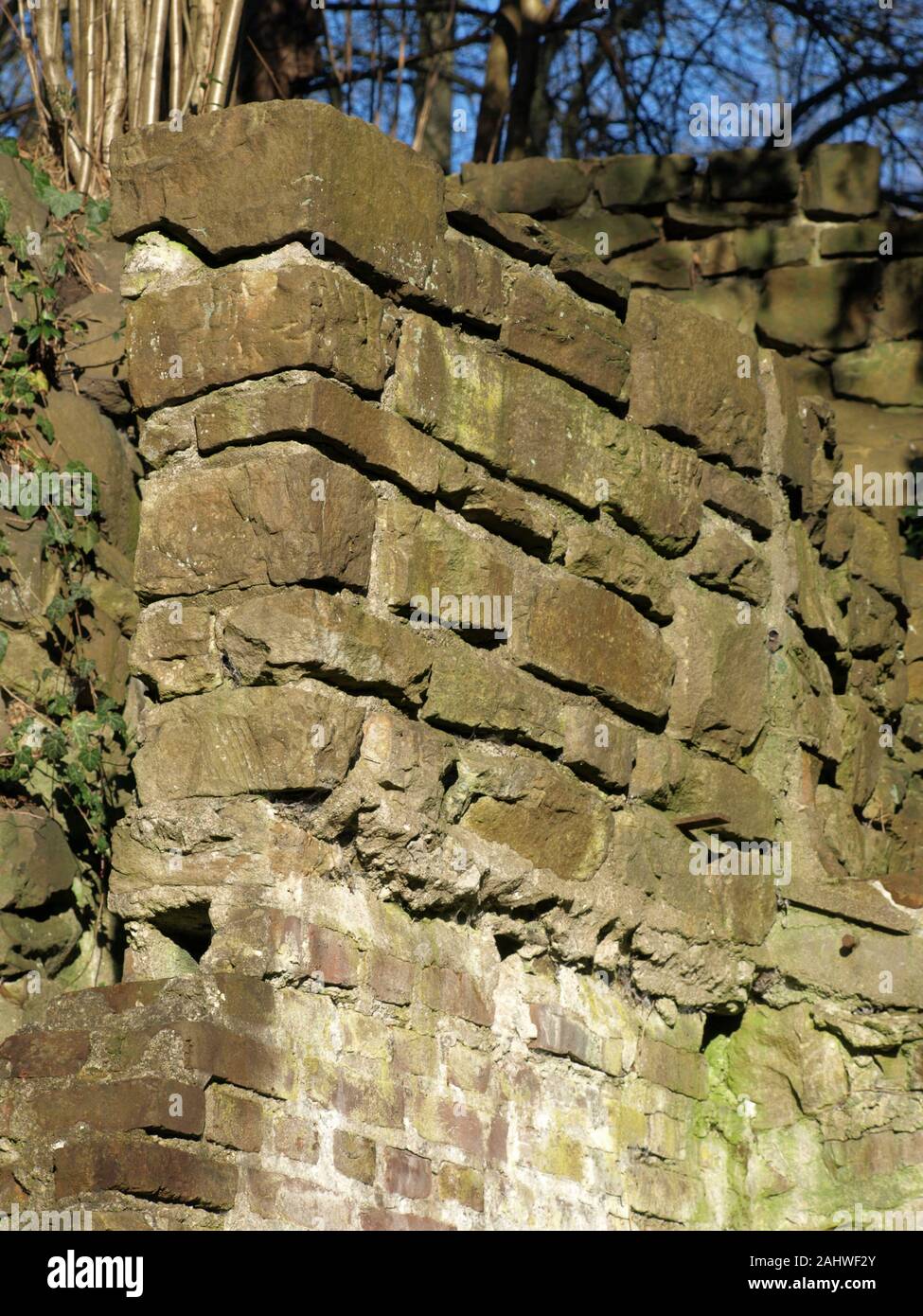 old quarry stone wall with a foundation of bricks. Blue sky and trees in the blurred background Stock Photo