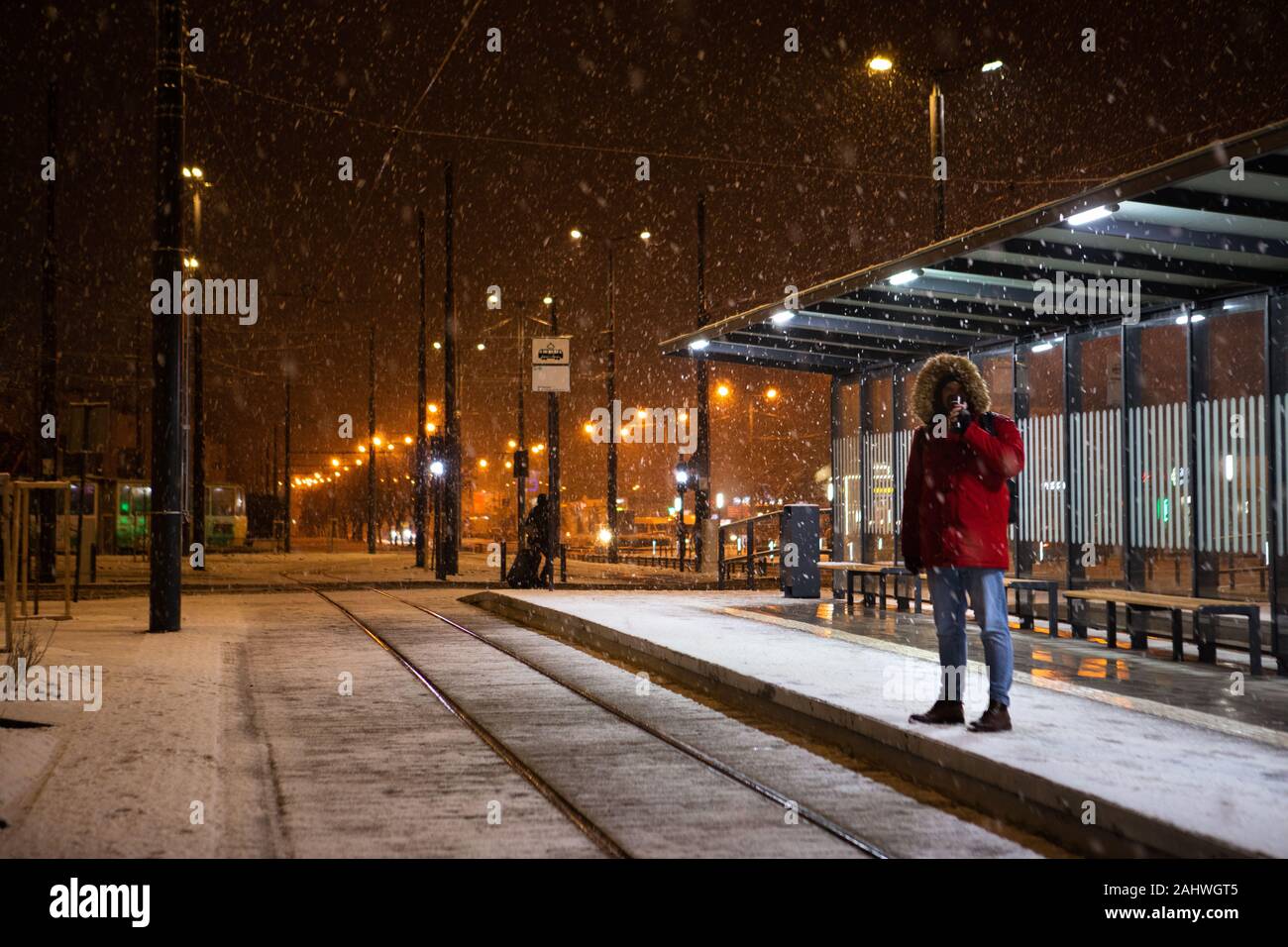man in red winter coat standing at bus tram stop waiting for public transport Stock Photo