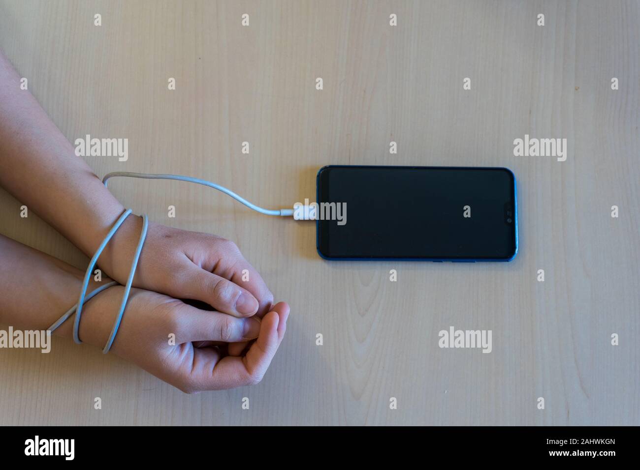 Woman's hands tied to the smartphone by the battery charging wire. Smartphone and technology addiction concept Stock Photo