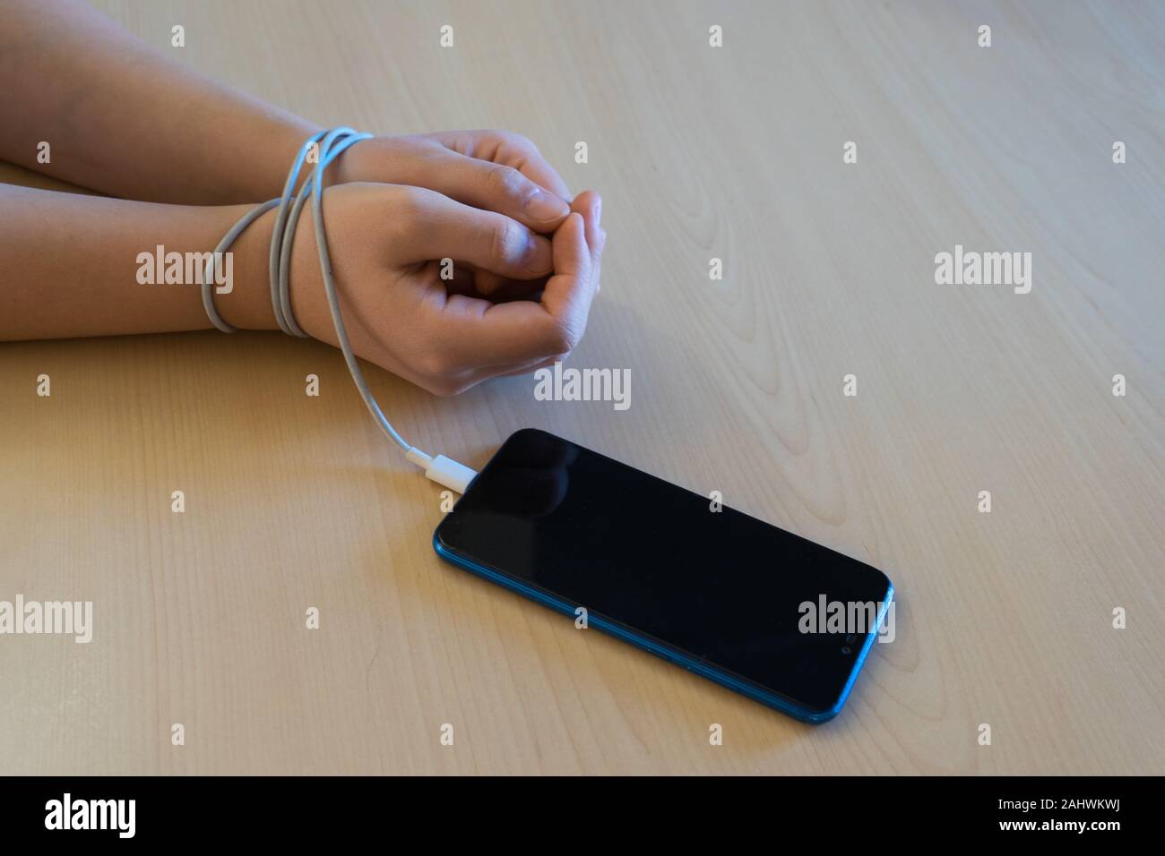 Woman's hands tied to the smartphone by the battery charging wire. Smartphone and technology addiction concept Stock Photo