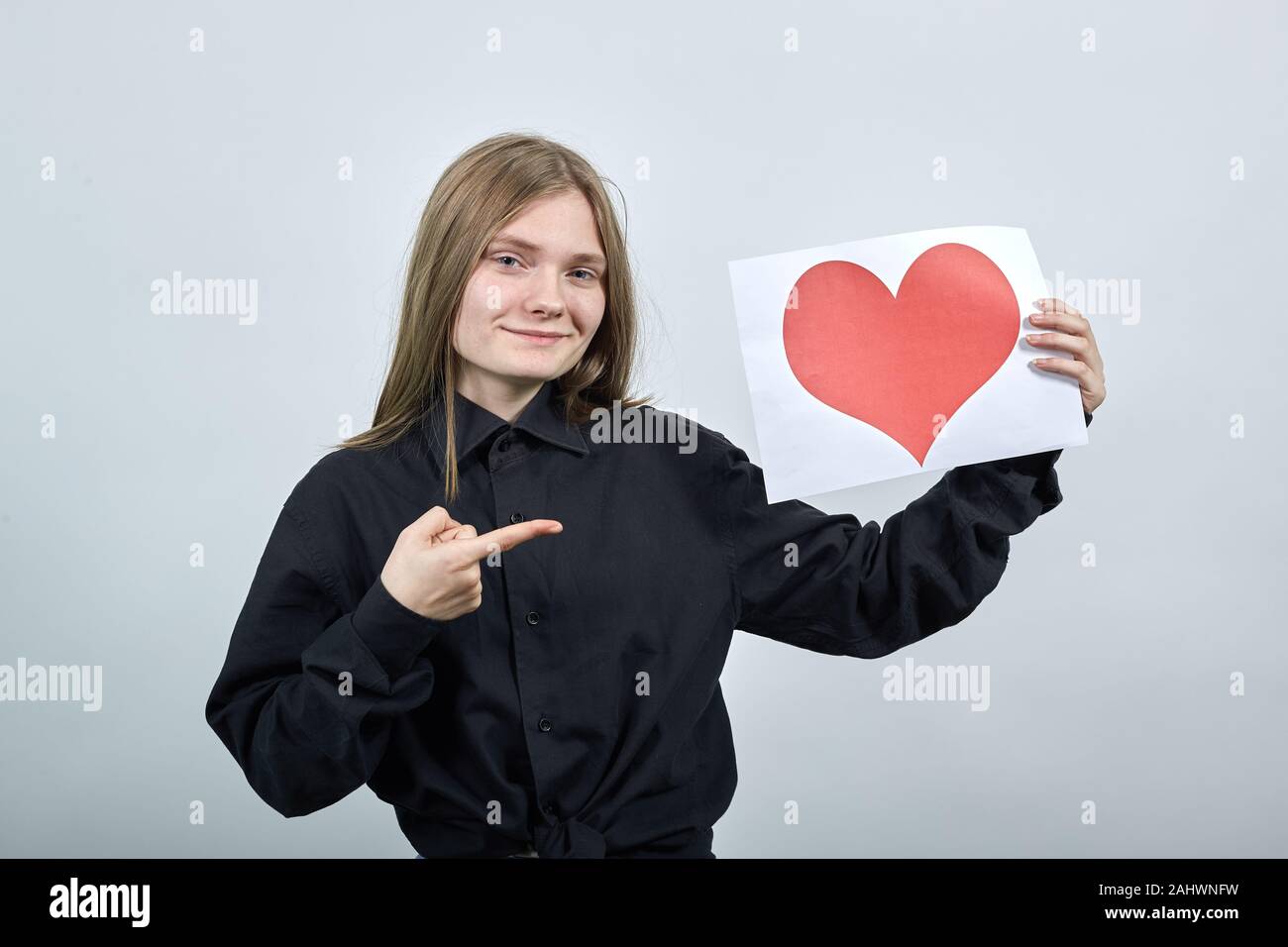 Charming woman keeping paper with picture of red heart, pointing finger ...