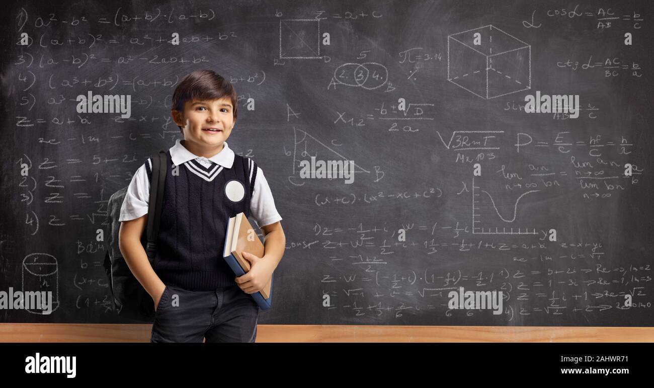 Schoolboy with books and backpack standing in front of a blackboard with math formulas Stock Photo