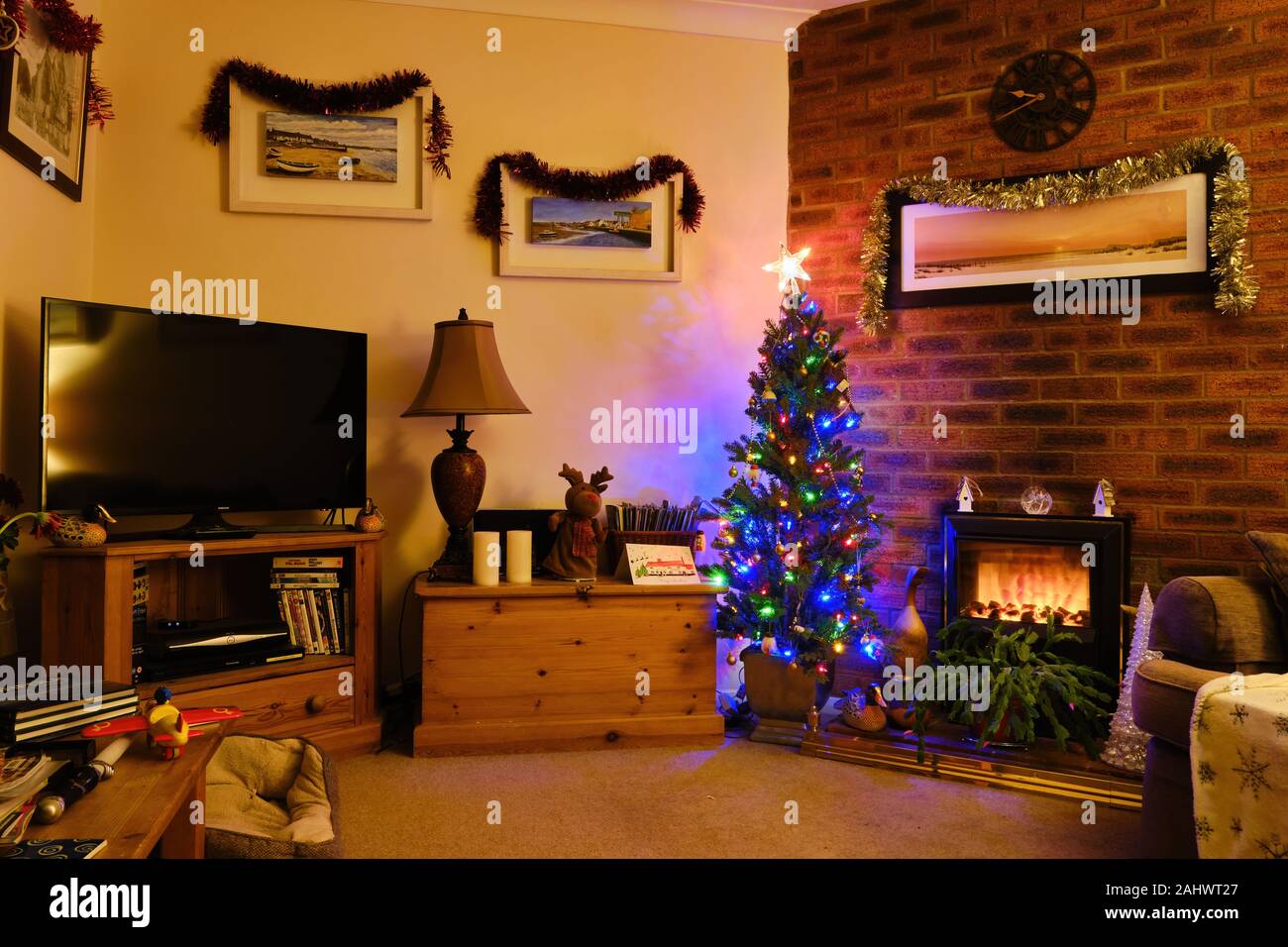 Festive Christmas Xmas decorations around a living room with tree fireplace with brick surround television and tinsel Stock Photo