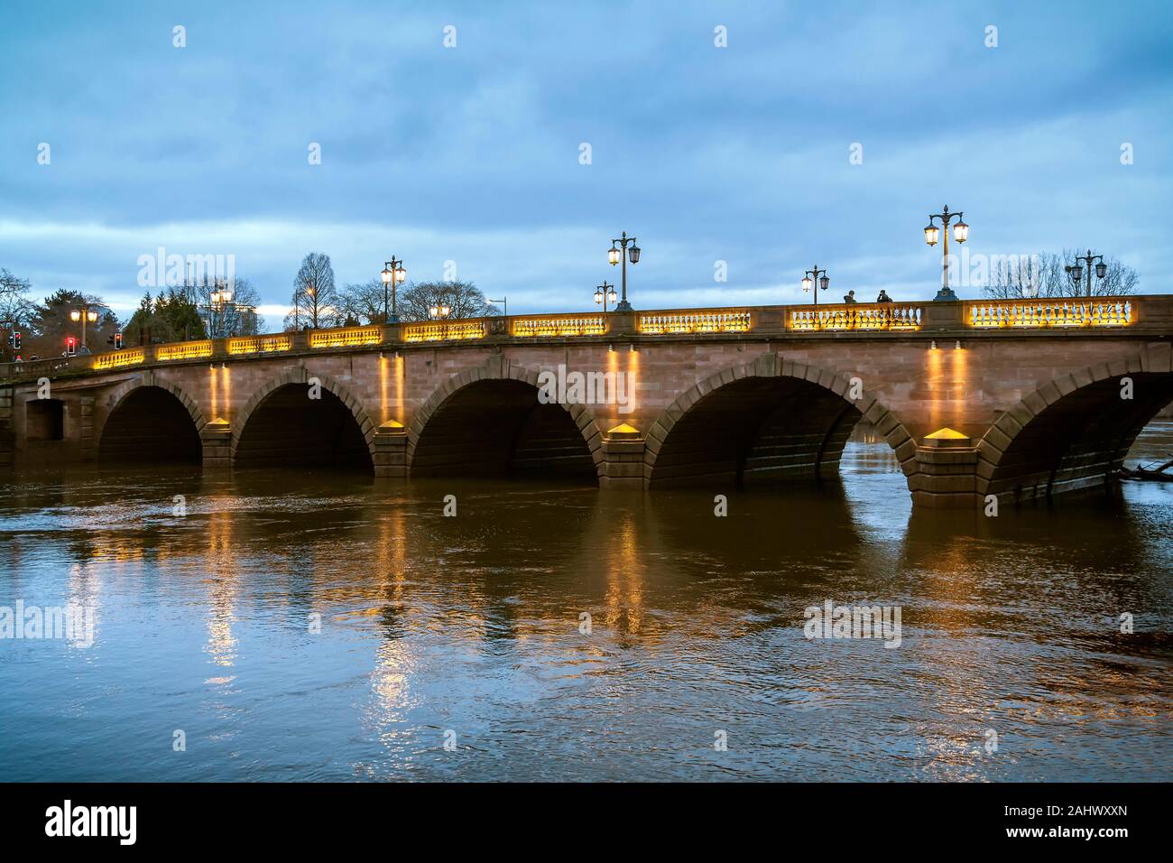 Worcester bridge at dusk. Traditional style lampposts light the magnificent arches of the bridge and reflect in the water of the River Severn below. Stock Photo